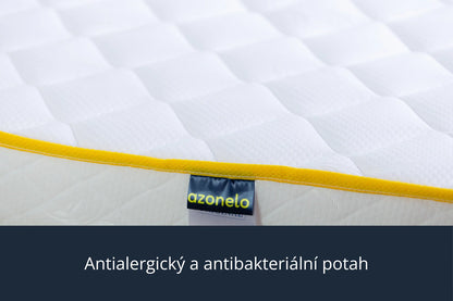Detailní záběr na čistý bílý potah s moderním žlutým lemováním a látkovou nášivkou s logem Azonelo. Materiál je měkký na dotek, prodyšný a upravený tak, aby byl vhodný pro alergiky.