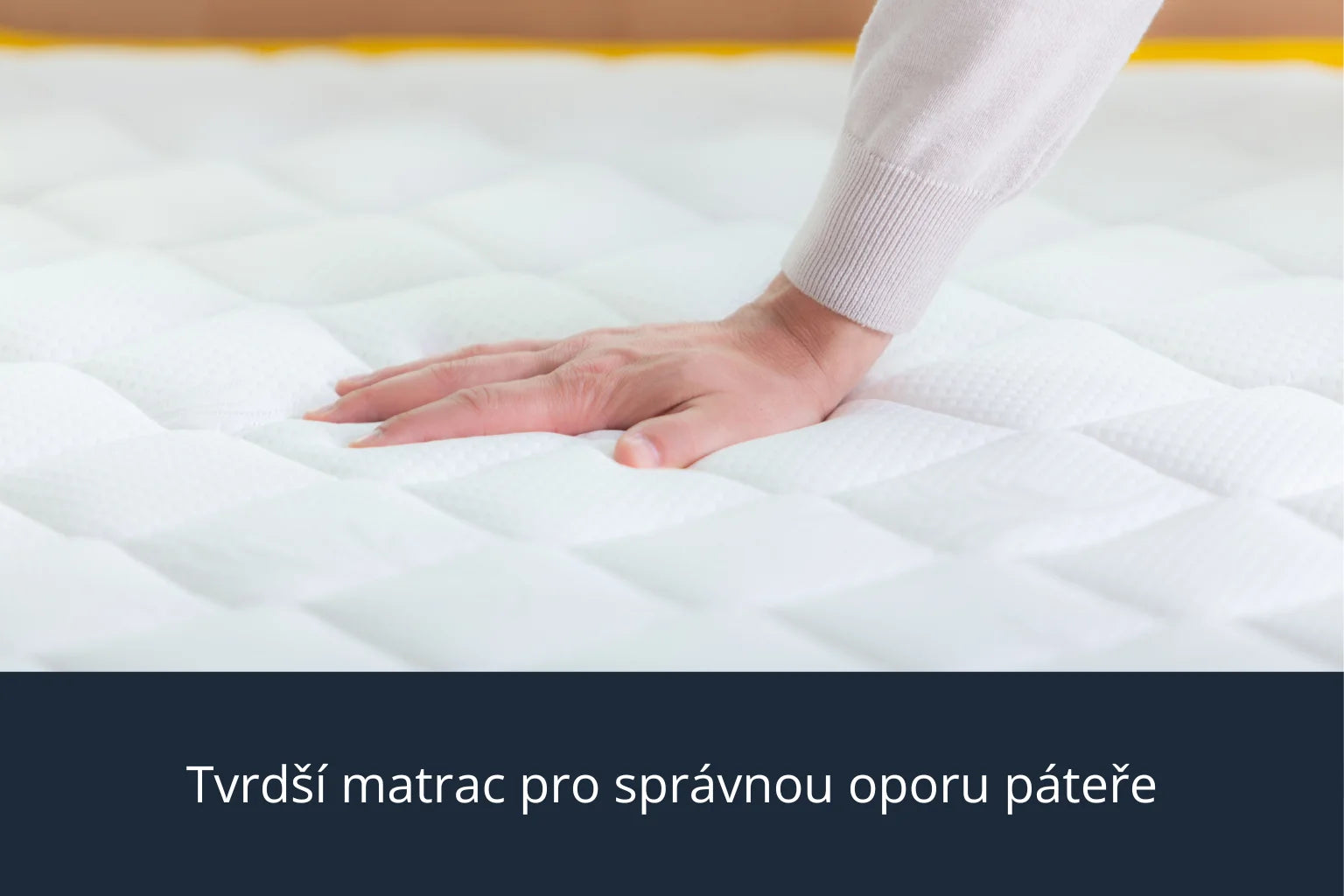 Pohled zblízka na ruku, která zatlačuje do bílého prošívaného matrace Azonelo Original. Obrázek ukazuje, že matrac je příjemně pevný, neprohýbá se a poskytuje spolehlivou oporu pro páteř.